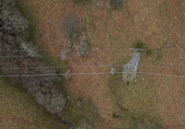 a large piece of barren land with little vegetation, a pylon, and cables